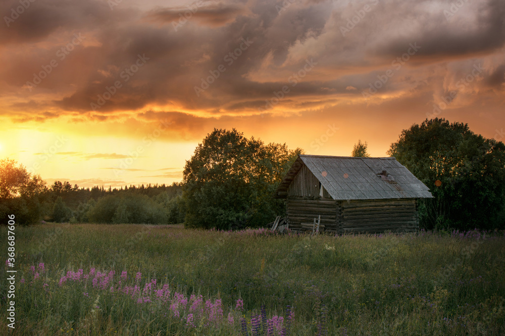 Rural landscape. Against the backdrop of the golden setting sun and huge leaden clouds there is a small, lonely hut. Summer. Dawn. Abandoned, old barn. Horizontal photo. Rural landscape. Against the backdrop of the golden setting sun and huge leaden clouds there is a small, lonely hut. Summer. Dawn. Abandoned, old barn. Horizontal photo.