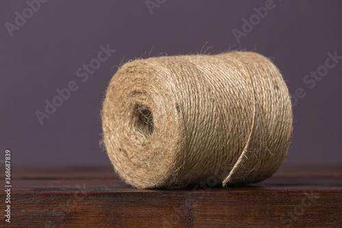 A large skein of brown twine lies on a wooden shelf on a plain background