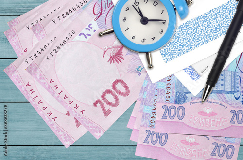 200 Ukrainian hryvnias bills and alarm clock with pen and envelopes. Tax season concept, payment deadline for credit or loan. Financial operations using postal service photo