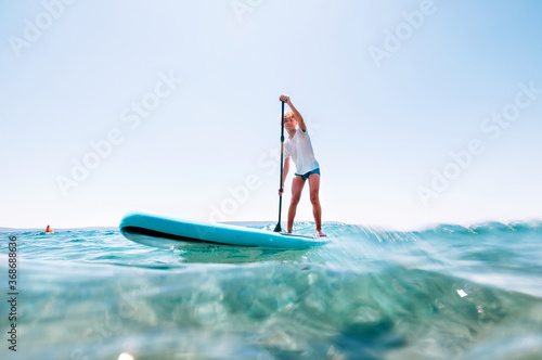 Under the water view angle to the smiling blonde teenager boy rowing stand up paddle board. Active family summer vacation time near the sea concept image. © Soloviova Liudmyla
