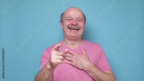 Senior hispanic man laughing at you, pointing finger to the camera