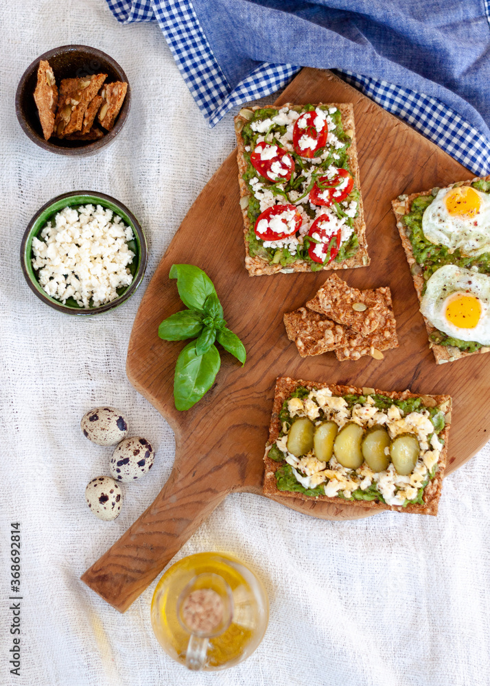 Healthy organic food. Avocado toast with greek cheese, cherry tomatoes with basil, fried eggs and cucumber. Colorful toast. Top view Healthy organic food. Avocado toast with greek cheese, cherry tomatoes with basil, fried eggs and cucumber. Colorful toast. Top view
