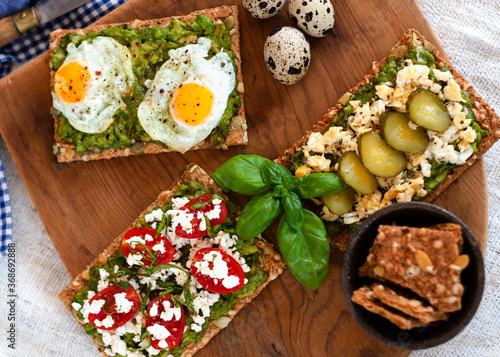 Colorful avocado toast with fried eggs, cucumber, cherry tomatoes and greek cheese, over a wooden cutting table. Rustic mood. Top view.