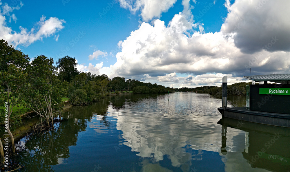 Beautiful view of a river and a wharf with reflections of blue sky, light clouds and trees on water, Parramatta river, Rydalmere, New South Wales, Australia