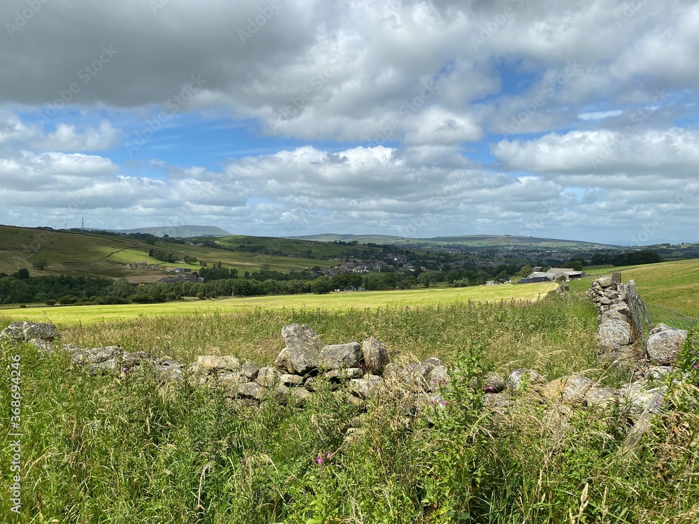 Looking over a dry stone wall, with fields, meadows, and a village in the distance near, Trawden, Colne, UK