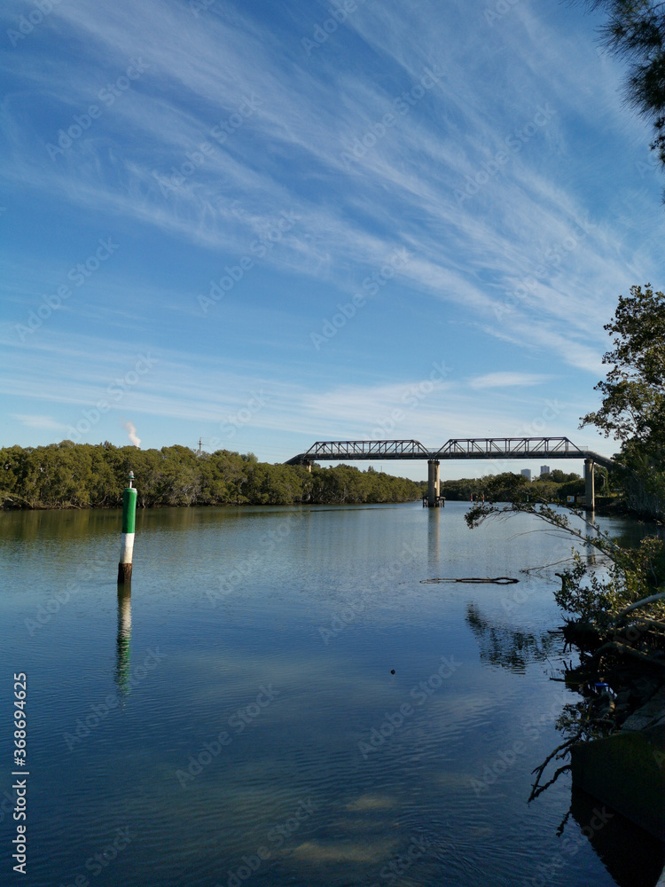 Fototapeta premium Beautiful view of a river with reflections of tall pedestrian bridge, trees and blue sky, Parramatta river, Rydalmere, New South Wales, Australia