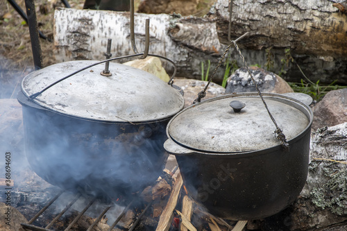 Metal cauldrons with lids are heated and smoked on a fire in the forest, tourist dishes for cooking. photo