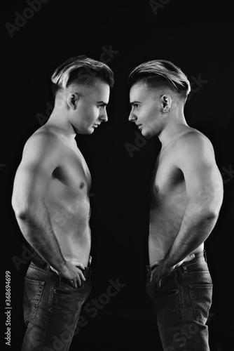 two twin brothers in blue jeans with a naked strong torso posing. black and white 