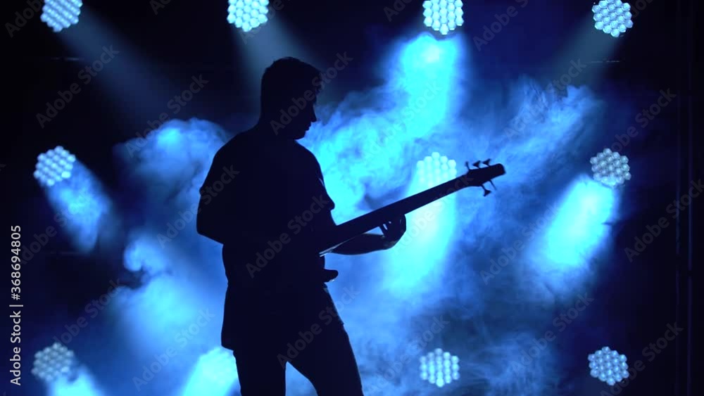 Silhouette of a young guy playing on the electric guitar on stage in a dark studio with smoke and neon lighting. Silhouette of a young guy playing on the electric guitar on stage in a dark studio with smoke and neon lighting.