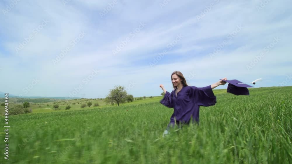 Graduation girl running alone in a green field with red tulips. Virtual graduation and social distancing concept.