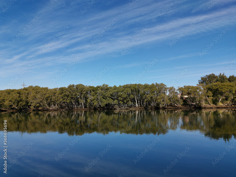 Beautiful view of a river with reflections of blue sky, light clouds and trees on water, Parramatta river, Rydalmere, New South Wales, Australia