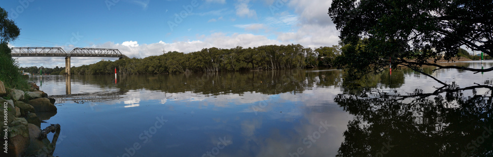 Beautiful panoramic view of a river with reflections of tall pedestrian bridge, trees and blue sky, Parramatta river, Rydalmere, New South Wales, Australia