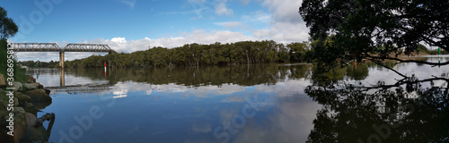 Beautiful panoramic view of a river with reflections of tall pedestrian bridge, trees and blue sky, Parramatta river, Rydalmere, New South Wales, Australia