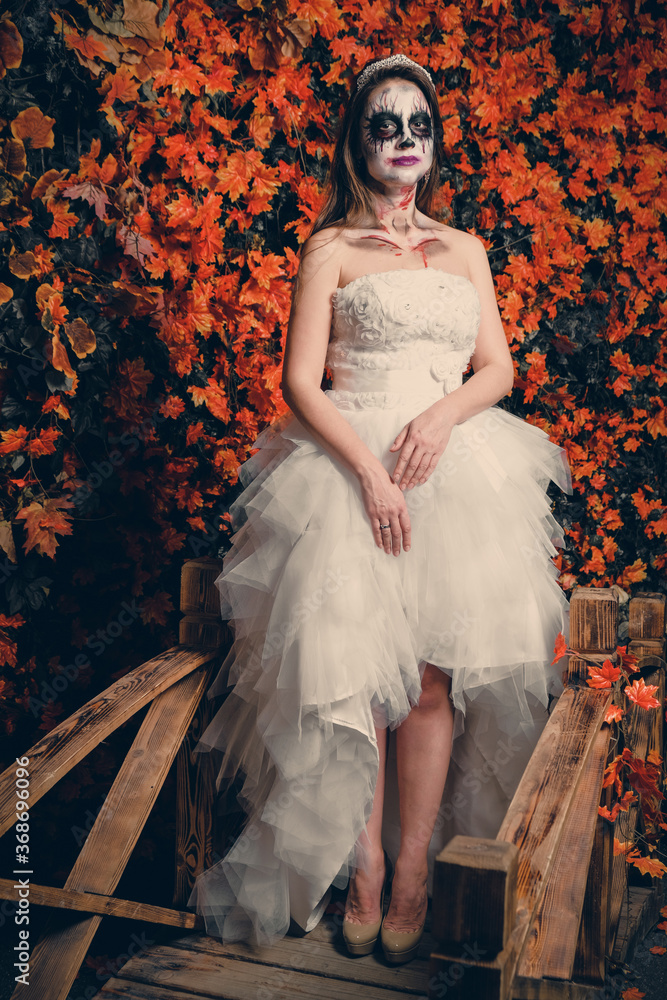 Woman with ghost make-up and wedding dress on yellow leaves background