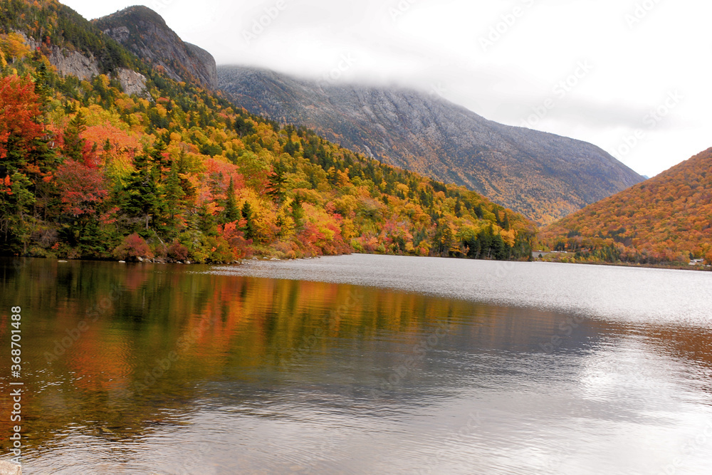 Autumn in White Mountains of New Hampshire. Sweeping view of Franconia Notch and colorful foliage from shore of Echo Lake. Dusting of snow on mountains and reflections of fall colors on lake. Autumn in White Mountains of New Hampshire. Sweeping view of Franconia Notch and colorful foliage from shore of Echo Lake. Dusting of snow on mountains and reflections of fall colors on lake.