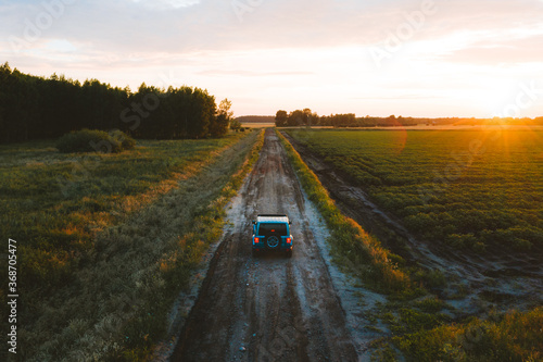Aerial view of suv vehicle driving on countryside road during sunset in summer.