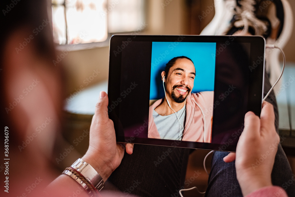 Young happy Latino man has a video call from a tablet with his girlfriend