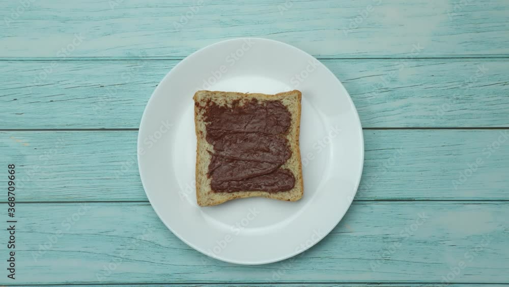 Eating toast with peanut butter, chocolate, Resting on a white ceramic plate on a wooden table Healthy breakfast concept 4K Stop motion food animation. Eating toast with peanut butter, chocolate, Resting on a white ceramic plate on a wooden table Healthy breakfast concept 4K Stop motion food animation.