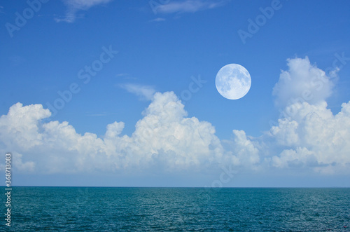 Bright white clouds and the moon in blue sky over green sea