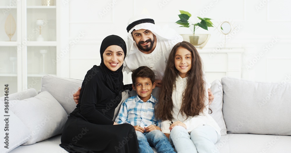 Portrait Of Cheerful Arabian Family With Two Kids Sitting On Couch And Portrait Of Cheerful Arabian Family With Two Kids Sitting On Couch And