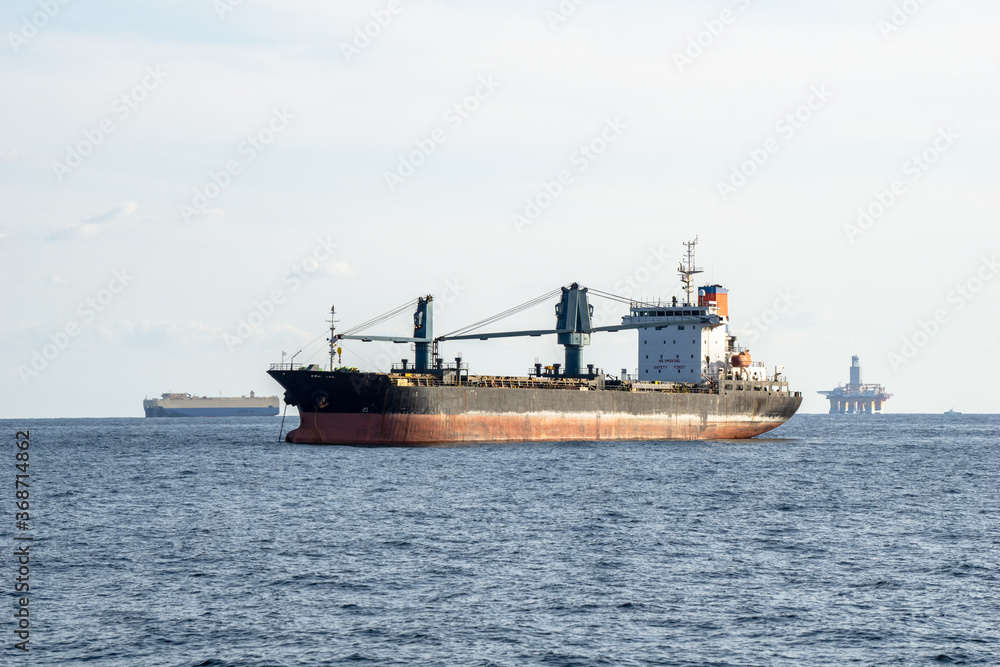 Old commercial cargo ship with heavy cranes anchors in the sea.