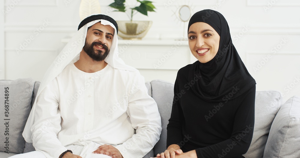 Arabs muslim happy couple talking to camera, waving with hands. Having videochat. Male and female Arabians videochatting on webcam. Middle East. Male in kandura and woman in hijab. Traditional outfits