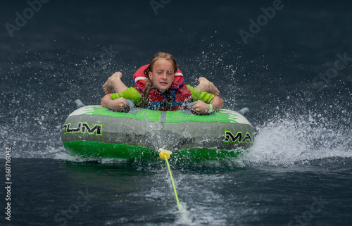 A girl being towed behind an inflatable sea biscuit on a lake with dark water