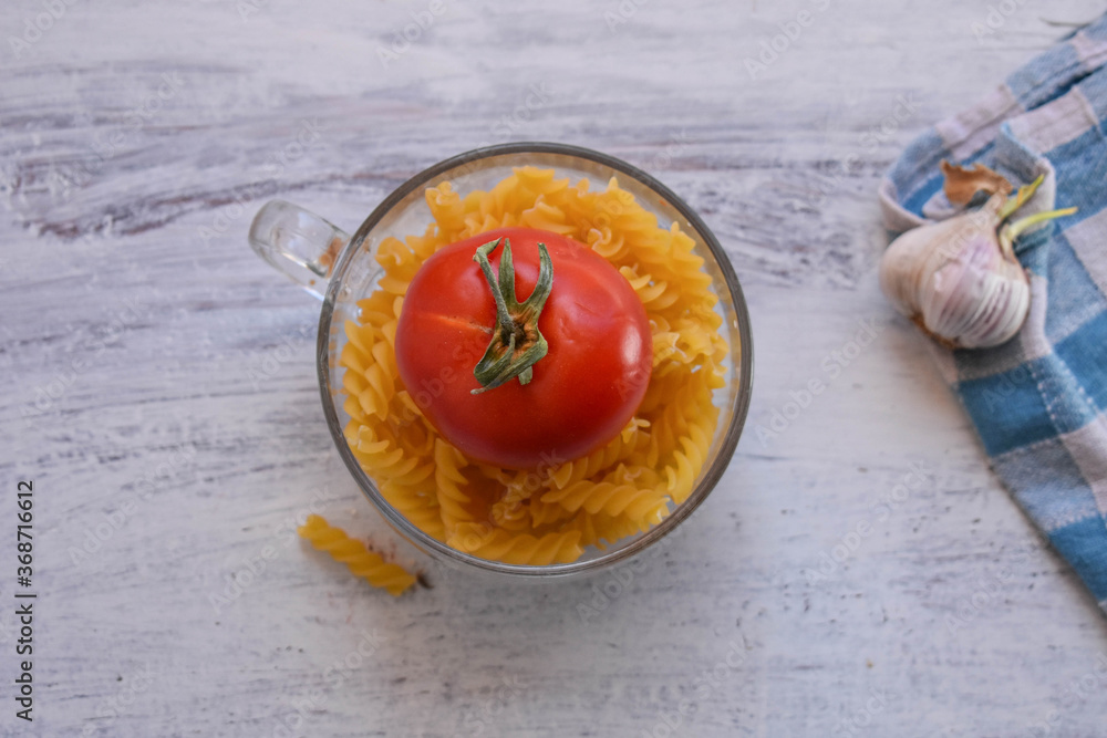 Products for cooking. Fresh red tomato, garlic and macaroni pasta at wooden table background/ kitchen- food- cooking background Products for cooking. Fresh red tomato, garlic and macaroni pasta at wooden table background/ kitchen- food- cooking background