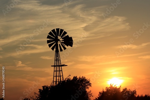 windmill at sunset with tree's,clouds, and the Sun north of Hutchinson Kansas USA out in the country.