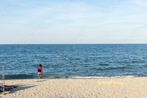 Young girl tourist enjoys playing with sea waves alone at a peaceful beach under blue cloudy sky on the afternoon