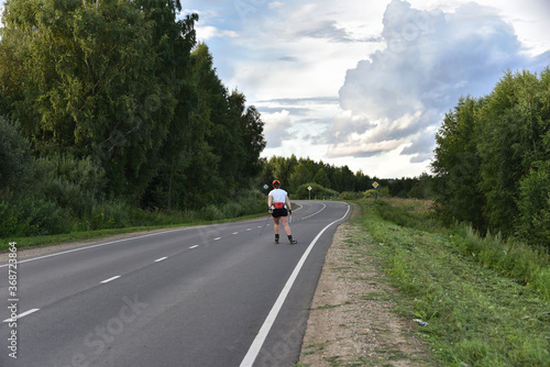 A woman on roller skis is rolling along an asphalt country road.