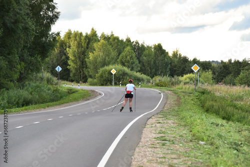 A woman on roller skis is rolling along an asphalt country road.