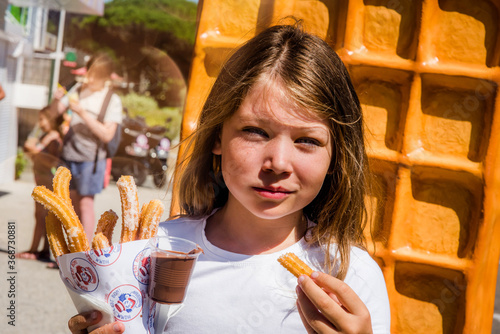 cute young girl devouring churros with chocolate