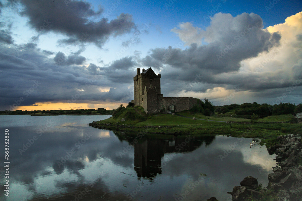 Dunguaire Castle spiegelt sich im Wasser bei Sonnenuntergang und dramatischen Wolken