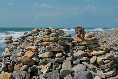 Boy playing, hiding behind a fortress of stones on the beach