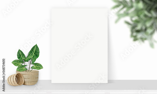 Interior vertical rectangular poster mockup standing on the table with plant and decorations on empty white wall background. Rendering illustration.