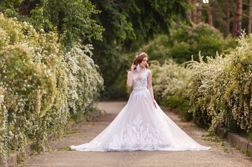 Foto Beautiful redhead Bride in fantastic wedding dress in blooming garden