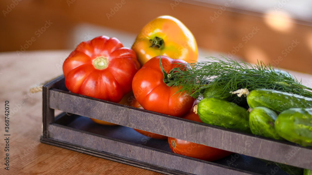 Vegetables tomatoes and cucumbers in a wooden box on a wooden table, close-up. Harvest, garden, vegetable garden. Blurred bokeh background.