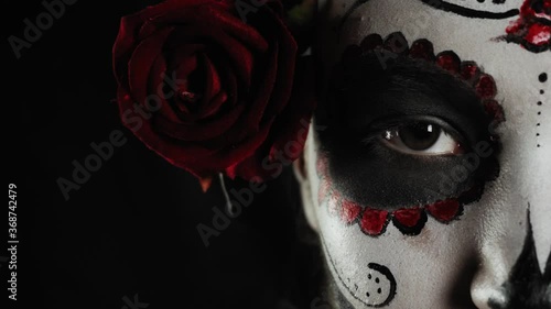 Mexican day of the dead. Young woman with sugar skull Halloween makeup looks at the camera with one eye. Extreme close-up. Happy Halloween. High quality 4k video
