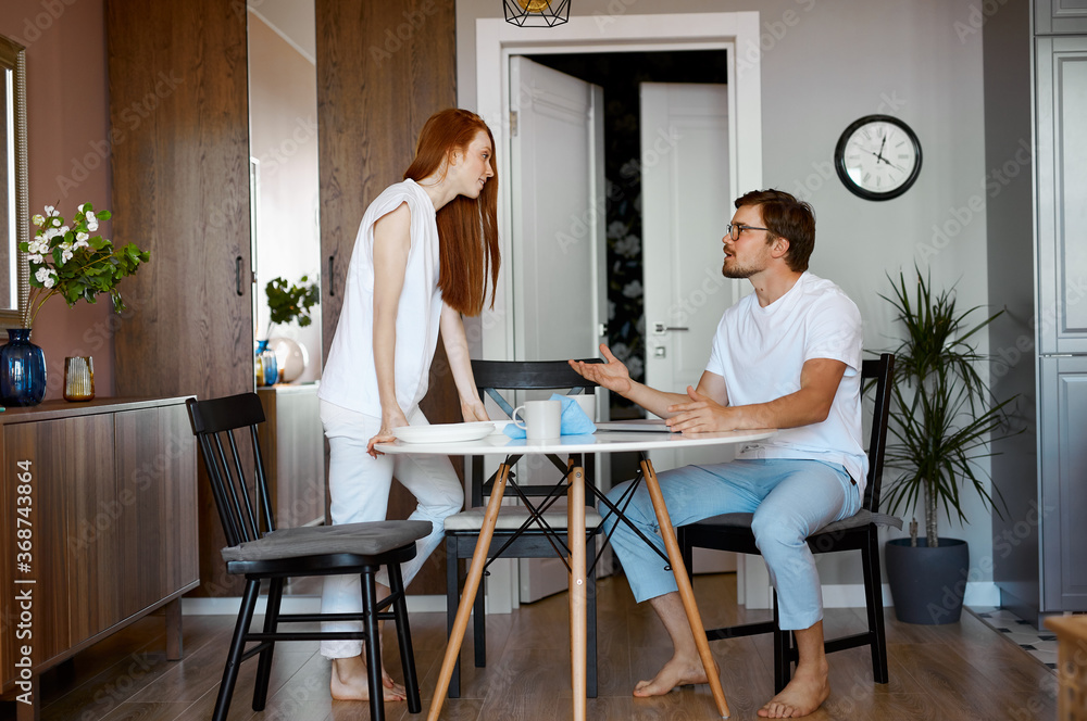 working man and redhead woman are swearing at home in the kitchen, girl expresses dissatisfaction while man sitting with laptop. man always plays online games working man and redhead woman are swearing at home in the kitchen, girl expresses dissatisfaction while man sitting with laptop. man always plays online games