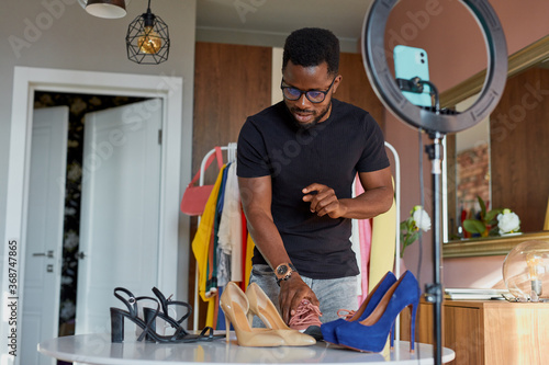 handsome black blogger man show purchase at camera, talk about female shoes and sneakers, give opinion. at home