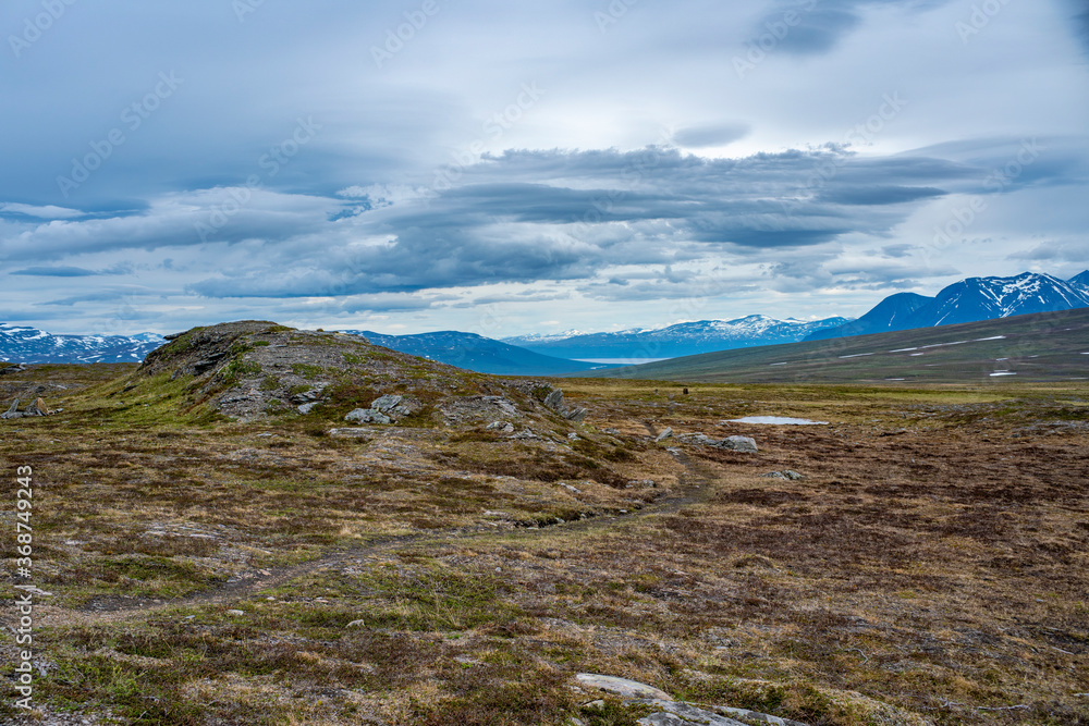 Mountain landscape and Wide Grassland Scenery in Padjelanta National Park with Wet Hiking Trail leading away from Camera during dramatic weather in the Summer in Northern Sweden, Lapland.