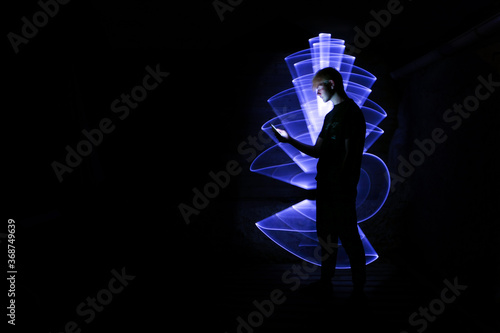 Silhouette of a man using a smartphone. Abstract shape at lightpainting with a light saber. Face illuminated by screen.	 photo