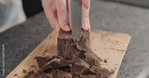 female hands breaking big dark chocolate block with knife on wood board