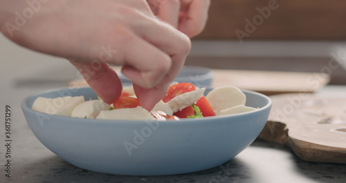 making salad with frisee lettuce, tomatoes amd mozzarella in a blue bowl on kitchen countertop