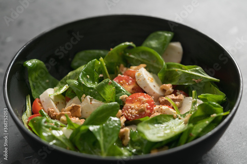 Salad with spinach, tomatoes and mozzarella in black bowl on concrete countertop