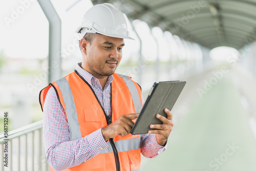 Asian civil engineer operate with tablet to control working at construction. Worker wearing hard hat at highway concrete road site.