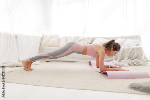 young sports girl in sportswear is doing yoga and stretching at home in a bright room.