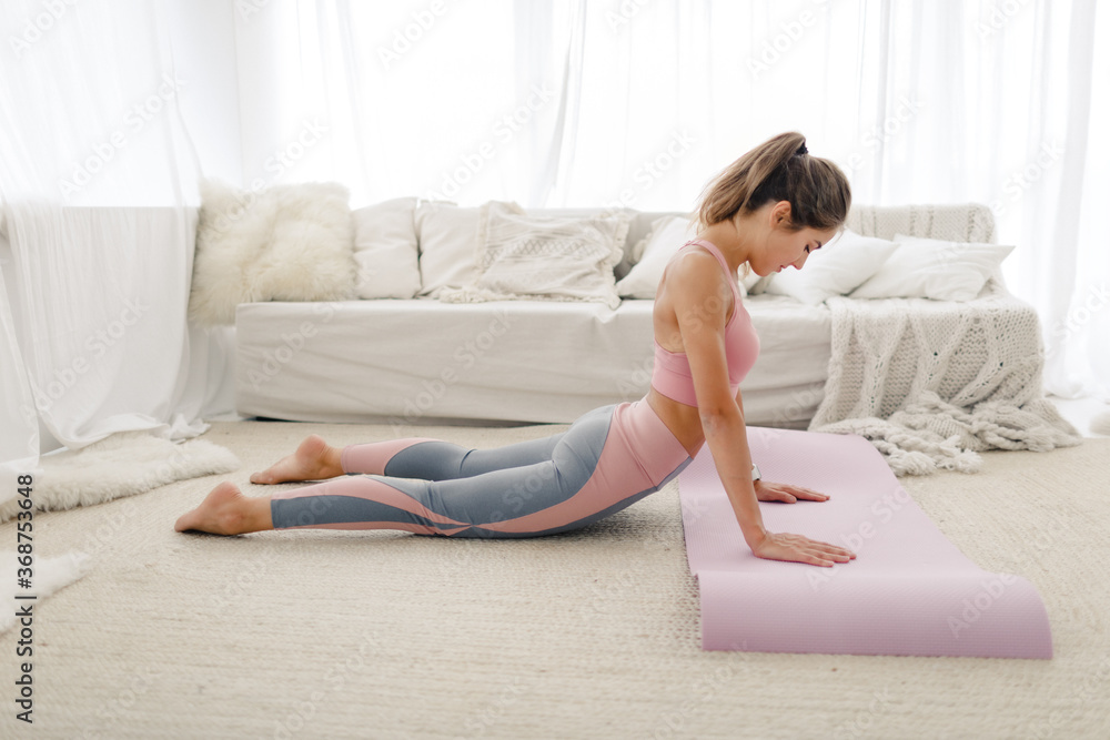young sports girl in sportswear is engaged in yoga and stretching at home. Does isolation exercises in a bright room. healthy lifestyle