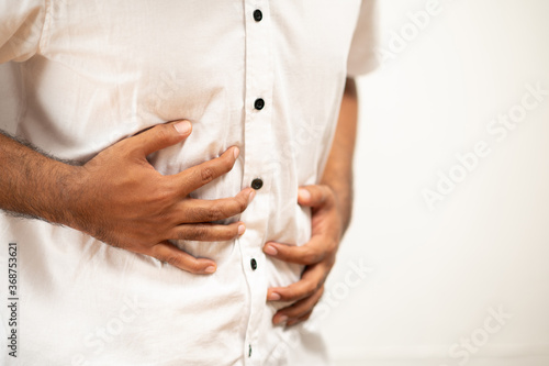 A man in white shirt with a stomach ache He squeezed his stomach with both hands. Because he ate bad and poisonous food he has go to toilet now.